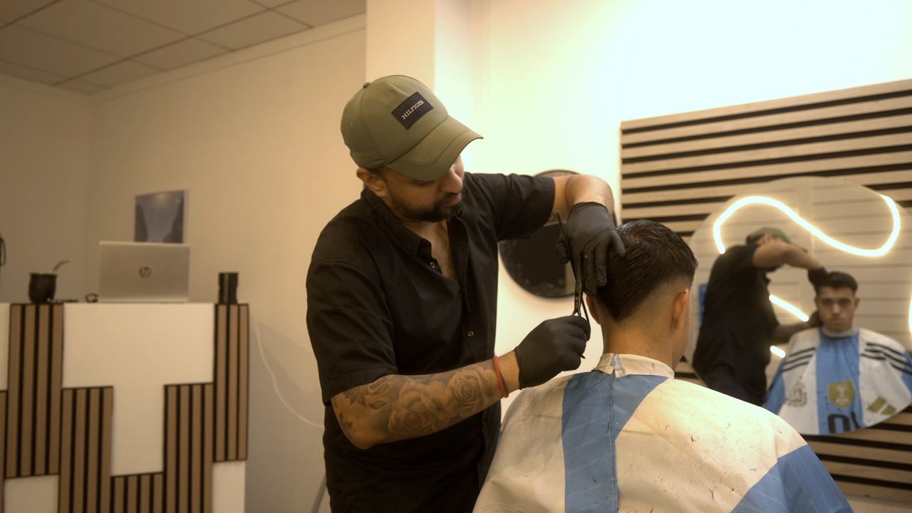 El peluquero corta el pelo a tijera y peine a un cliente con la capa de Argentina